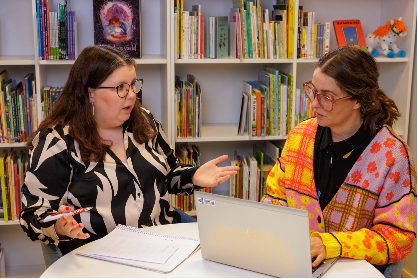 Linnea och Jonna diskuterar vid en laptop i ett bibliotek